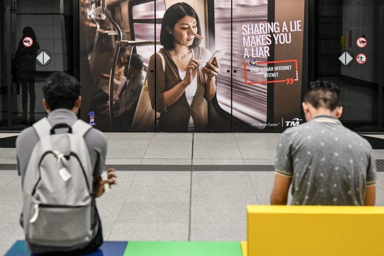 Commuters wait for the train in-front of an advertisement reading "Sharing a lie makes you a liar" at a train station in downtown Kuala Lumpur on March 26, 2018.